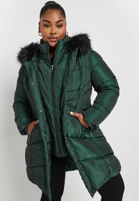Grön puffjacka med en glänsande yta, huva med fuskpäls, dragkedja framtill och två sidofickor. Den quiltade designen ger struktur.