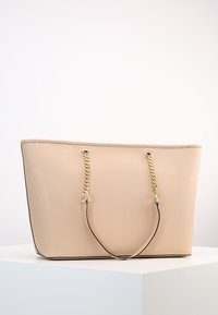 Borsa tote beige in materiale sintetico, con manici in catena dorata, texture liscia e bordi scuri a contrasto.