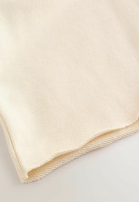 Tissu en coton crème avec une texture douce et lisse. L'ourlet présente un bord brut avec un détail tricoté en bas.