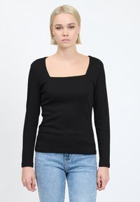 Top nero a maniche lunghe con scollatura quadrata, texture a coste e silhouette aderente, abbinato a jeans blu.