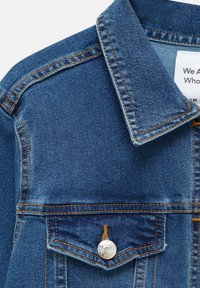 Veste en jean bleu foncé avec surpiqûres orange, col pointu et poche poitrine boutonnée avec fermeture à pression en métal argenté.