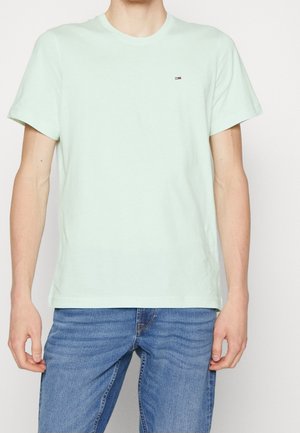 Miętowo zielony bawełniany t-shirt z okrągłym dekoltem, krótkimi rękawami i małym logo, zestawiony z niebieskimi dżinsami.