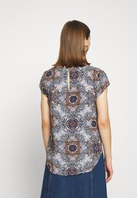Blusa de manga corta con un colorido patrón floral y geométrico. El material es ligero, con un dobladillo redondeado y un detalle de ojal en la parte posterior.