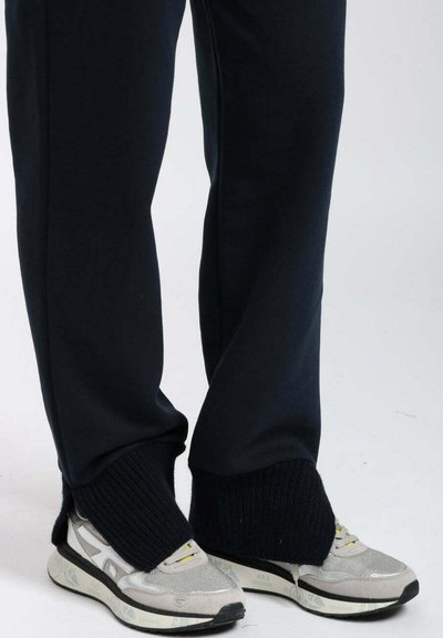 Scarpe da ginnastica grigie con tomaia in mesh e suole bianche, abbinate a pantaloni della tuta blu navy con orlo a costine e polsini alle caviglie.