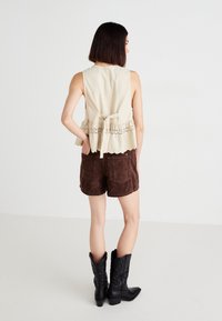 Beige sleeveless top with ruffled hem and lace detail, paired with brown suede shorts and black cowboy boots with decorative stitching.