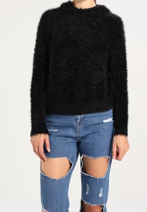 Schwarzer, fusseliger Pullover mit langen Ärmeln und rundem Halsausschnitt, kombiniert mit ausgewaschenen blauen Jeans mit großen Knieauschnitten und fransigen Säumen.