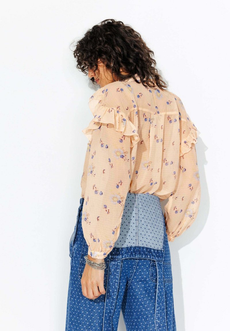 Blouse à motifs floraux de couleur pêche avec des manches volantes, associée à un jean taille haute à pois bleus. Tissu doux et léger.