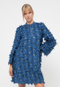 Blå kjole prydet med stoffblomster og utsmykninger, med krage, lange ermer og en løs passform, med en teksturert overflate.