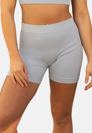 Frau trägt hellgraue, gerippte Biker-Shorts mit hoher Taille und passendem kurzen Oberteil, steht mit einer Hand auf dem Oberschenkel.