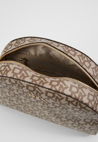 Ruskea ja kreemukuvioitu meikkipussi, jossa on kaksi vetoketjua, sisätasku ja kultaiset metalliosat. Edessä on logo.