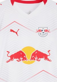 Camiseta de fútbol blanca con detalles en rojo, que presenta un cuello en V, rayas diagonales y el logo del RB Leipzig con toros rojos y un círculo amarillo.