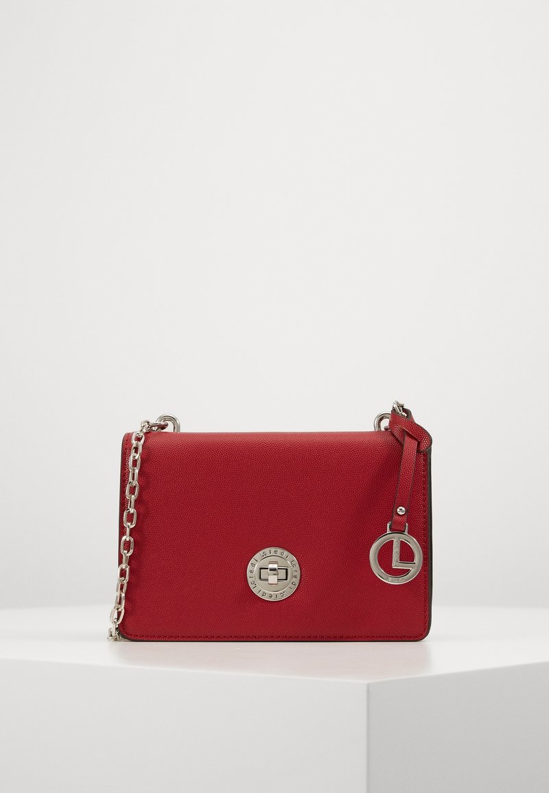 Punainen synteettinen käsilaukku, jossa on teksturoitu pinta, hopeiset yksityiskohdat, ketjuhihna ja pyöreä logo-yksityiskohta edessä.