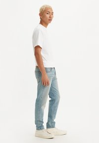 Vaqueros de denim de color azul claro con corte ajustado, combinados con una camiseta blanca lisa y zapatillas blancas. Diseño sencillo sin logotipos visibles.