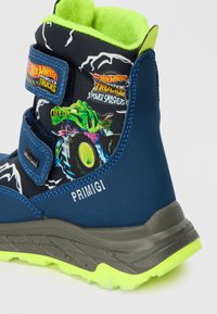 Botte d'enfants bleue en matériau synthétique, dotée d'une doublure en polaire verte, d'une semelle grise et de motifs graphiques de camions monstres. Bandes auto-agrippantes.