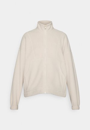Giacca in pile di colore beige chiaro con colletto alto, zip frontale e spalle cadute. Presenta un tessuto testurizzato e polsini a costine.