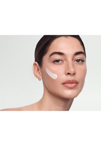 Foreslået hudplejeprodukt påført som en glat, hvid creme på modellens kind. Huden har en naturlig tone med subtil tekstur og glans.