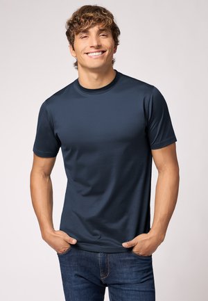 Donkerblauwe t-shirt met korte mouwen en ronde hals, gemaakt van soepele stof, gedragen met de handen in de zakken, gecombineerd met blauwe spijkerbroek.