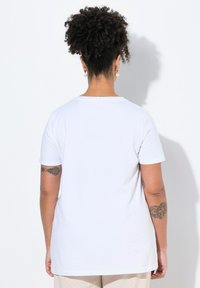Camiseta blanca de manga corta con cuello redondo. Material suave y corte relajado. Presenta tatuajes visibles en los brazos.