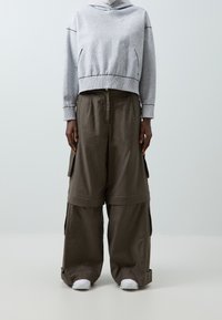 Grå kort hoodie med ett texturerat mönster och vita accenter, ihop med vida, olivgröna cargobyxor med sidfickor. Vita sneakers.