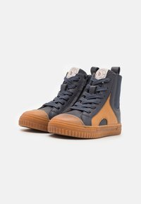 Zapatillas altas en cuero color navy oscuro y marrón, con una suela de goma texturizada, diseño de cordones y cremallera lateral para un fácil uso.
