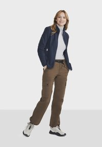 Veste en polaire marine avec poches zippées, associée à un pantalon cargo marron avec poches latérales. Portée avec des baskets gris clair.