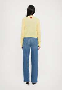 Gul lett gensere med lange ermer, kombinert med høyt liv blå rette jeans med baklommer og subtile sømdetaljer.
