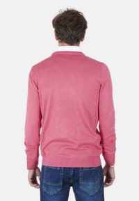 Maglione rosa lavorato a maglia con scollo a V e polsini e orlo a coste, abbinato a jeans di denim blu. Il materiale sembra morbido e leggero.