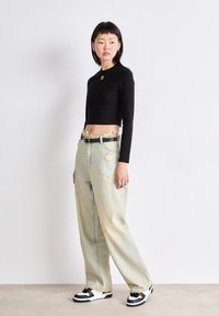 Schwarzes, kurzes Langarmoberteil, hellblaue, ausgefranste, weit geschnittene Jeans mit fransigem Saum und schwarz-weiße Sneaker mit Schnürdetails.
