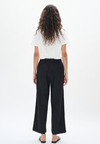 Svarta vida byxor med elastisk midja, i kombination med en enkel vit t-shirt med kort ärm. Slät tyg, minimalistisk design och avslappnad passform.