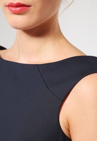 Marinstretch klänning utan ärmar med en strukturerad axeldesign, som har en slät tygtextur och en ren hantverkslinje.