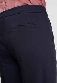 Marinblå byxor med en slät textur, featuring en enkel bakficka med en smal öppning och en åtsittande midja.