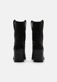 Bottines en suède noir avec un talon carré, dotées de tirettes à l'arrière et d'une texture lisse.