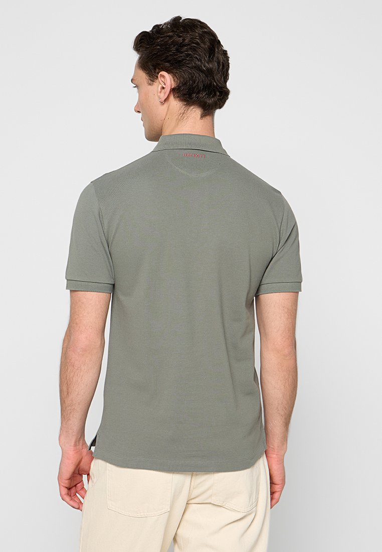 Collared polo shirt in muted olive green, short sleeves, textured fabric, featuring a subtle logo detail in red at the back.