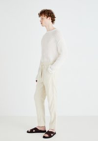 Sweter w kolorze kremowym, jasnobeżowe spodnie z elastycznym pasem i ciemnobrązowe sandały z krzyżującymi się paskami. Czysty, minimalistyczny design.
