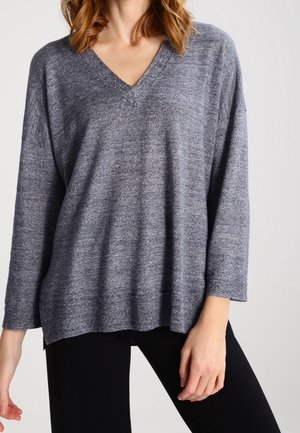 Maglione grigio a maglia testurizzata con scollo a V e maniche larghe. La vestibilità over si abbina a pantaloni neri per un look casual.