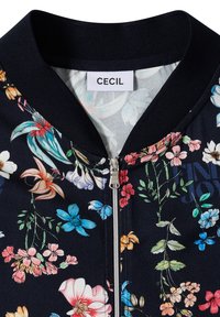 Veste bleu marine à motif floral avec col côtelé, fermeture éclair argentée et étiquette « CECIL » à l'intérieur de l'encolure.