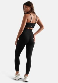 Completo sportivo nero a coste composto da un top corto con spalline regolabili e leggings a vita alta, abbinato a scarpe da ginnastica leggere.