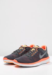 Šedé sportovní boty s oranžovými akcenty. Prodyšný síťovaný svršek, polstrovaná podešev a reflexní logo. Zaoblená špička a šněrovací design.