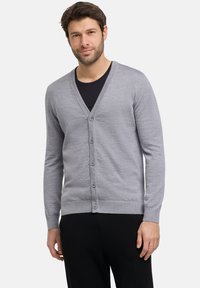 Cardigan grigio realizzato in morbido tessuto a maglia, con scollo a V, chiusura con bottoni e polsini e orlo a costine. Indossato sopra una maglietta nera.