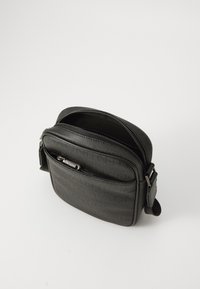 Sac bandoulière synthétique noir avec une finition texturée, des compartiments zippés et une bandoulière réglable. Présente un motif de logo en relief.