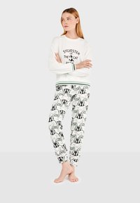 Weißer Pullover mit "Sylvester der Kater" Druck, grüne Akzente an den Bündchen. Die Schlafanzughose zeigt ein wiederholtes schwarz-weißes Muster mit Sylvester-Gesichtern.