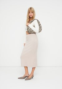 Un haut blanc en tricot à manches longues, une jupe beige mi-longue, des chaussures à talons gris et un sac à motif crocodile, tous présentés sur un fond uni.