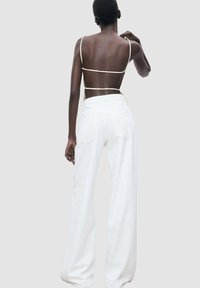 White wide-leg pants with a high waist, paired with a minimalist beige strappy top. Smooth fabric texture, tailored back pockets visible.