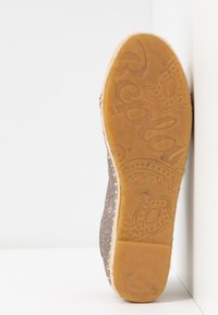 Semelle en caoutchouc marron avec le nom de la marque en relief. La tige présente une surface grise texturée et pailletée, avec un bout arrondi et un profil bas.