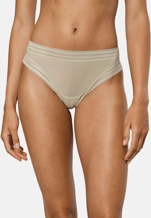 Sous-vêtement féminin beige taille haute avec bordure en dentelle sur la ceinture et les ouvertures des jambes, porté par un modèle debout sur un fond uni.