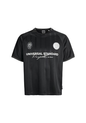 Maglia nera a maniche corte realizzata in tessuto liscio. Presenta righe verticali, toppe con logo e il bold bianco con la scritta "UNIVERSAL STANDARD."