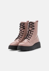 Bottines en cuir verni rose, avec des lacets noirs, une semelle épaisse noire et un détail de fermeture éclair sur le côté. Présente un léger talon et un bout rond.