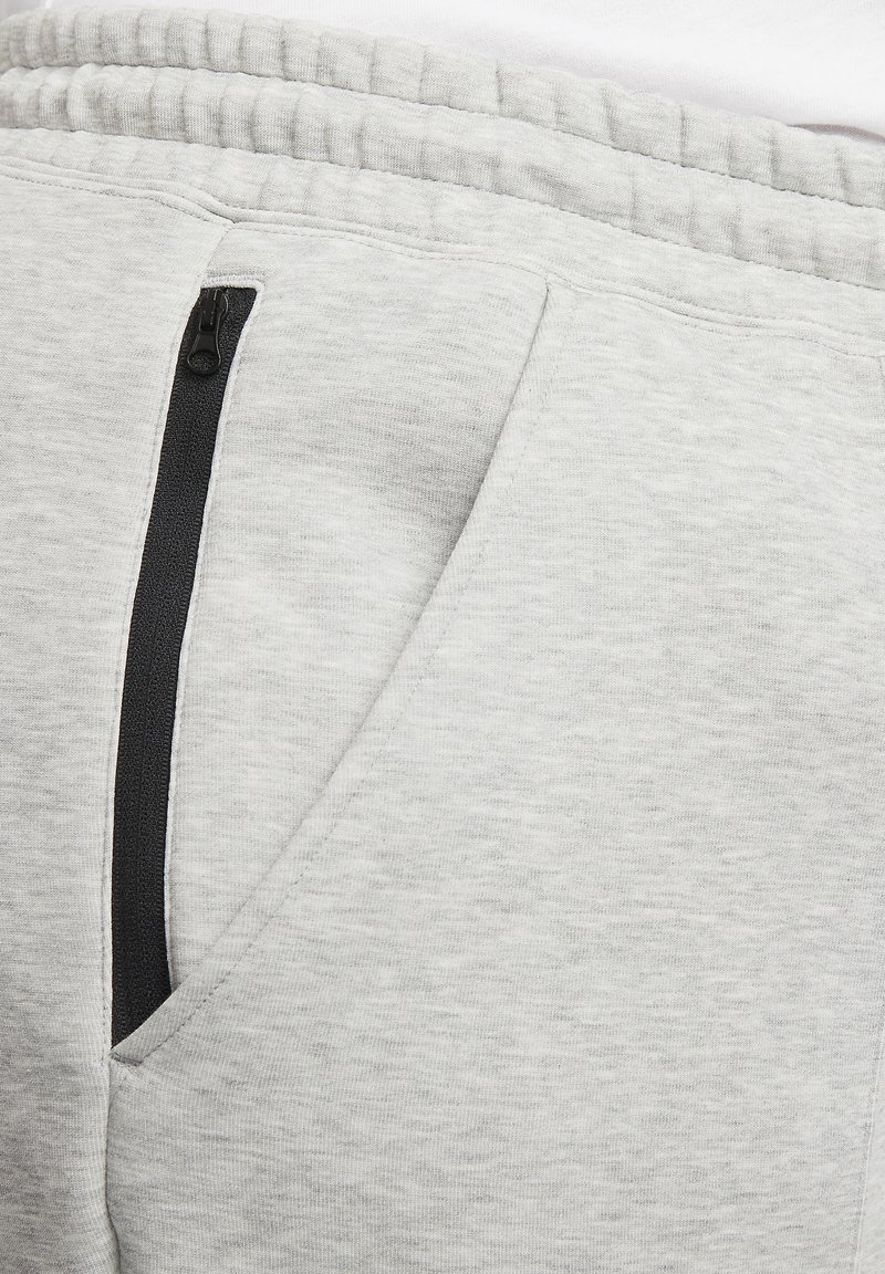 Helle graue Sweatpants mit einer weichen Textur, ausgestattet mit einer Reißverschlusstasche mit schwarzem Akzent und einem elastischen Bund.