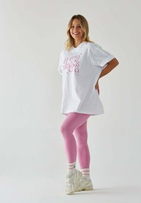 Biała, oversize t-shirt z różowym napisem, w połączeniu z różowymi legginsami. Akcesoria to białe sneakersy i w paski skarpetki. Gładkie faktury tkanin.