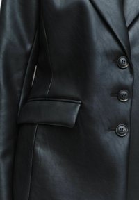 Svart läderblazer med skräddarsydd design, urklippta slag och runda svarta knappar. Inkluderar en ensam bröstficka.